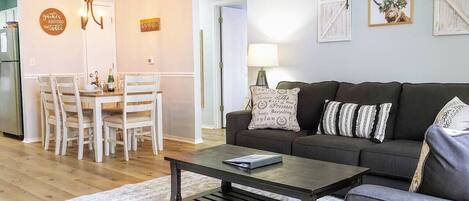 Un salon avec un canapé foncé, une table basse et un coin repas comprenant une table et des chaises en bois.