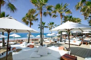 A beachside resort with white lounge chairs and umbrellas, palm trees, and a view of the ocean.