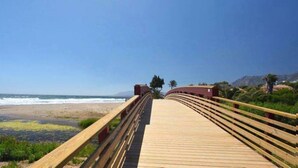 A wooden boardwalk leading to a beach with a clear view of the ocean and distant mountains.