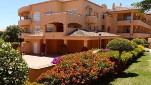 A multi-story building with balconies, a covered patio area, and a well-maintained garden with colorful flowers.