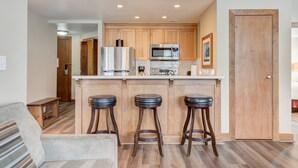 Une cuisine moderne avec des meubles en bois, des appareils électroménagers en acier inoxydable et trois tabourets de bar.