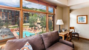 A hotel room with a large window, a brown sofa, a table with a lamp, and a framed picture on the wall.