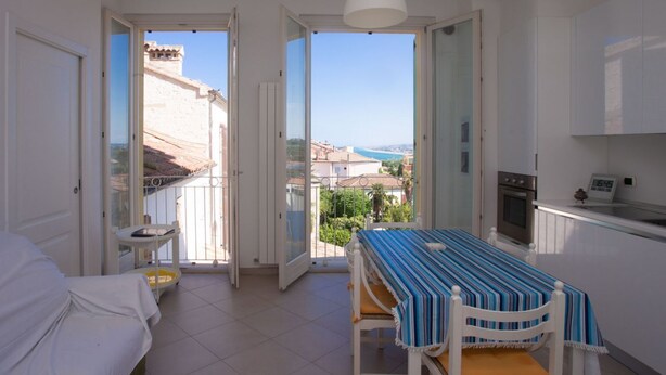 A room with a bed, a dining table with chairs, a kitchen area, and a balcony with a view of the city. - N236 Numana, two-room apartment with sea view in the heart of the town (Numana)