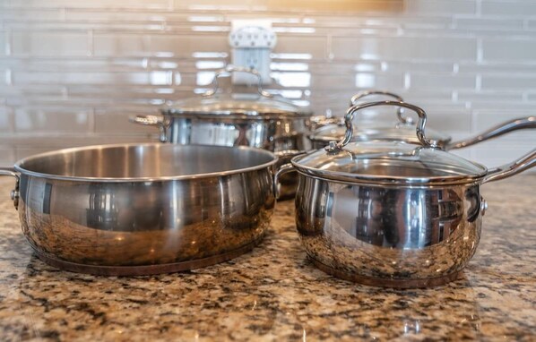 Stainless steel cookware with lids on a granite countertop.