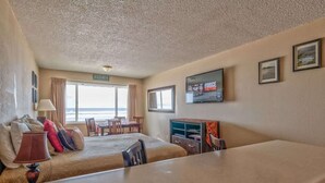 A hotel room with a bed, a desk, a TV, and a view of the beach. - Comfy Second Floor Beachfront Condo - Sleeps 4 - Pool and Sauna! (Lincoln City)