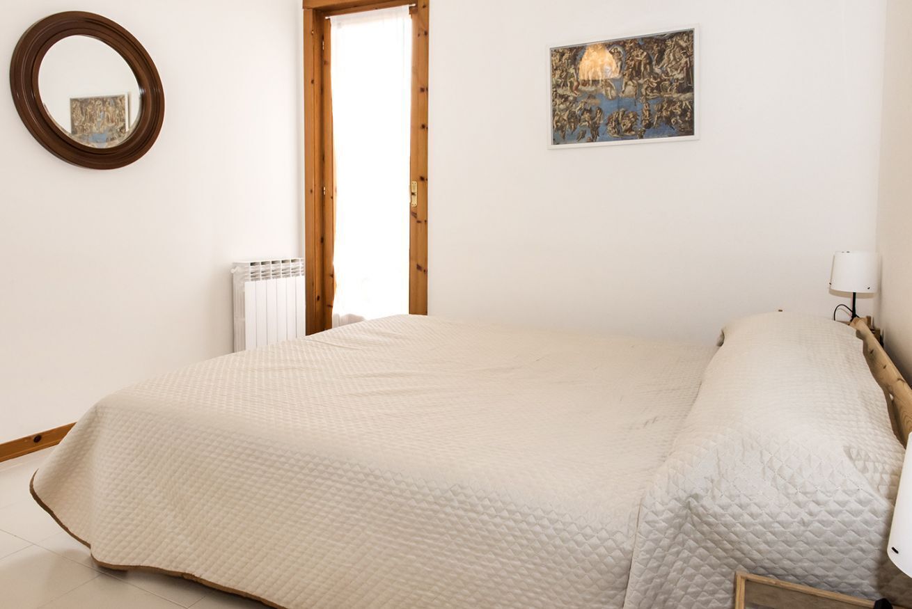 Une chambre à coucher avec un grand lit, un miroir rond, un radiateur et une œuvre d’art encadrée accrochée au mur.