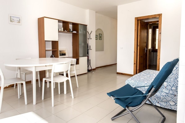 A modern kitchen with white cabinets, a dining table with chairs, and a blue patterned sofa.