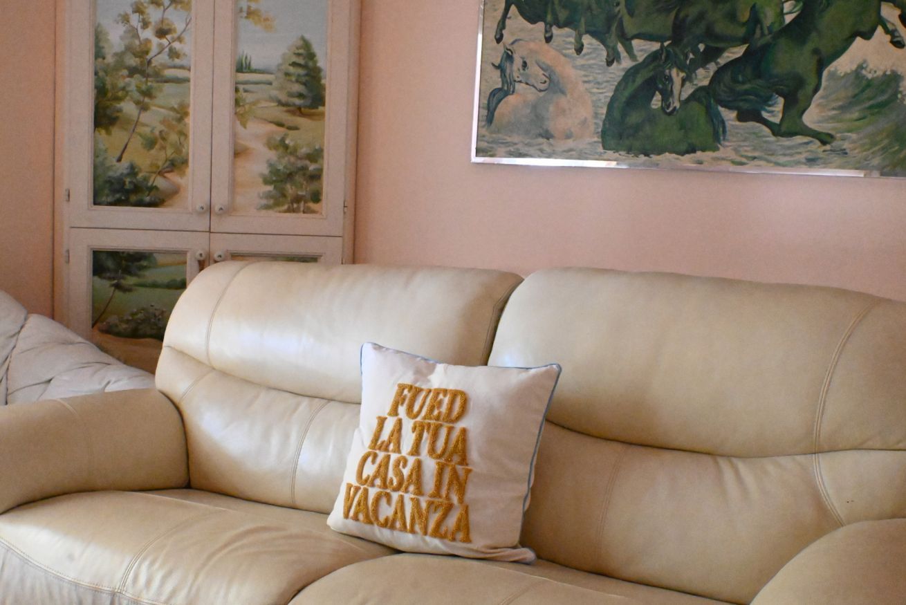 A beige leather sofa with a cushion that reads 'FUED LA TUA CASA IN VACANZA'.