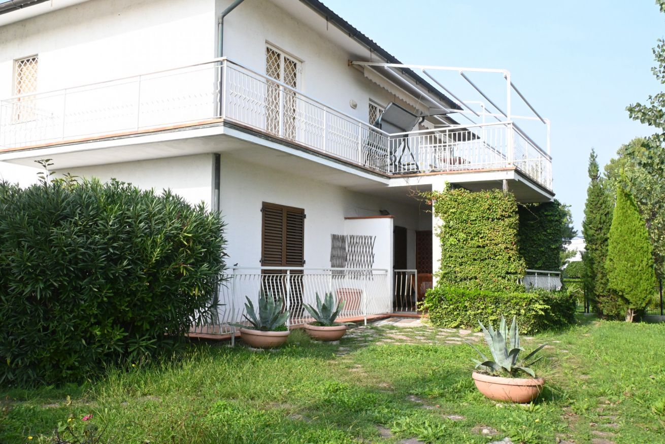 A two-story building with a balcony, potted plants, and a well-maintained garden.