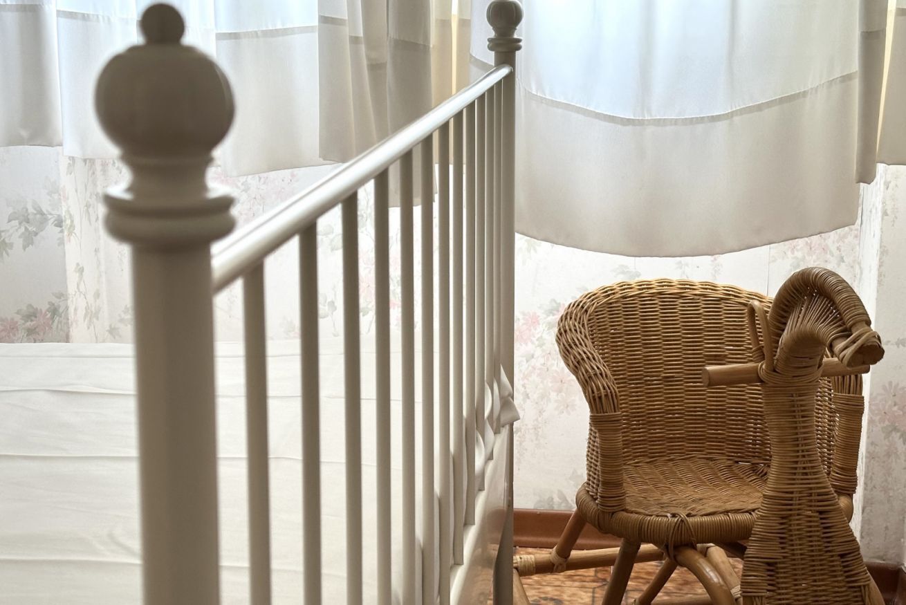 Eine Treppe mit weißer Brüstung führt zu einem Raum, der ein Korbstuhl und ein Fenster mit transparenten Vorhängen beinhaltet.