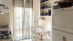 A kitchen with a dining table, chairs, a refrigerator, and shelves with kitchenware. - M292 - Marcelli, four-room apartment with garden 50 meters from the sea (Marcelli)