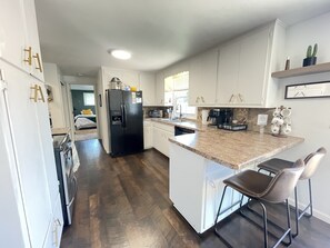 A modern kitchen with white cabinets, a black refrigerator, granite countertops, and a small island with bar stools.