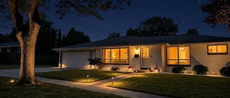 A residential house at night with illuminated windows and a well-maintained lawn.