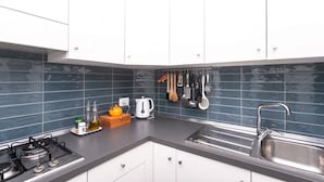 Een moderne keuken met witte kastjes, een gasfornuis, een spoelbak en verschillende keukengerei aan de wand.