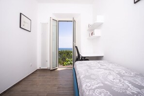 Un dormitorio con cama, un radiador, una puerta que da a un balcón y un estante con objetos.