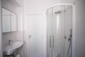 Un baño moderno con ducha envuelta en vidrio, un lavabo blanco y un armario con espejo.