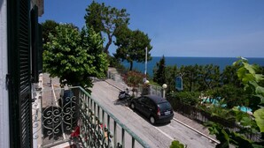 Een balkon met uitzicht op zee, een geparkeerde auto en een scooter.