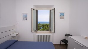 Een slaapkamer met een bed, een stoel, een bureau, een raam met uitzicht en een radiator.