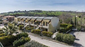 A multi-story building with a flat roof, surrounded by greenery and a parking area. - N036 - Numana, two-room apartment with terrace in residence with swimming pool (Maratta)