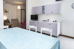 A room with a bed, a TV, a small kitchen area, and a dining table.