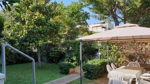 Un patio con mesa y sillas, rodeado de vegetación y un sendero.