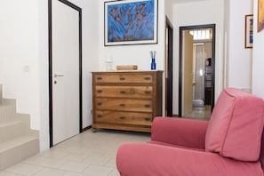 A room with a wooden dresser, a pink sofa, a staircase, and a framed artwork on the wall.