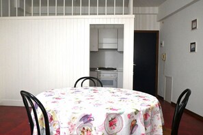Un comedor con una mesa redonda cubierta con mantel floral, sillas negras y una cocina al fondo.