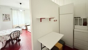 Una habitación compacta con una mesa de comedor, sillas, una mesita blanca y un refrigerador.
