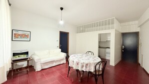 Un espacio habitable compacto con una mesa de comedor, un sofá, un televisor sobre un mueble bajo y una zona de cocina.
