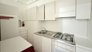 Una cocina con gabinetes blancos, estufa a gas, un lavamanos y una encimera.