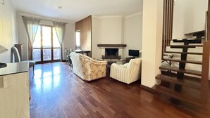 Een ruime woonkamer met een open haard, een eettafel en een trap.