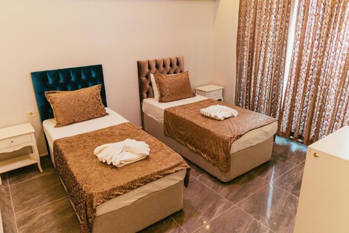 A hotel room with two beds, a nightstand, and a curtain.