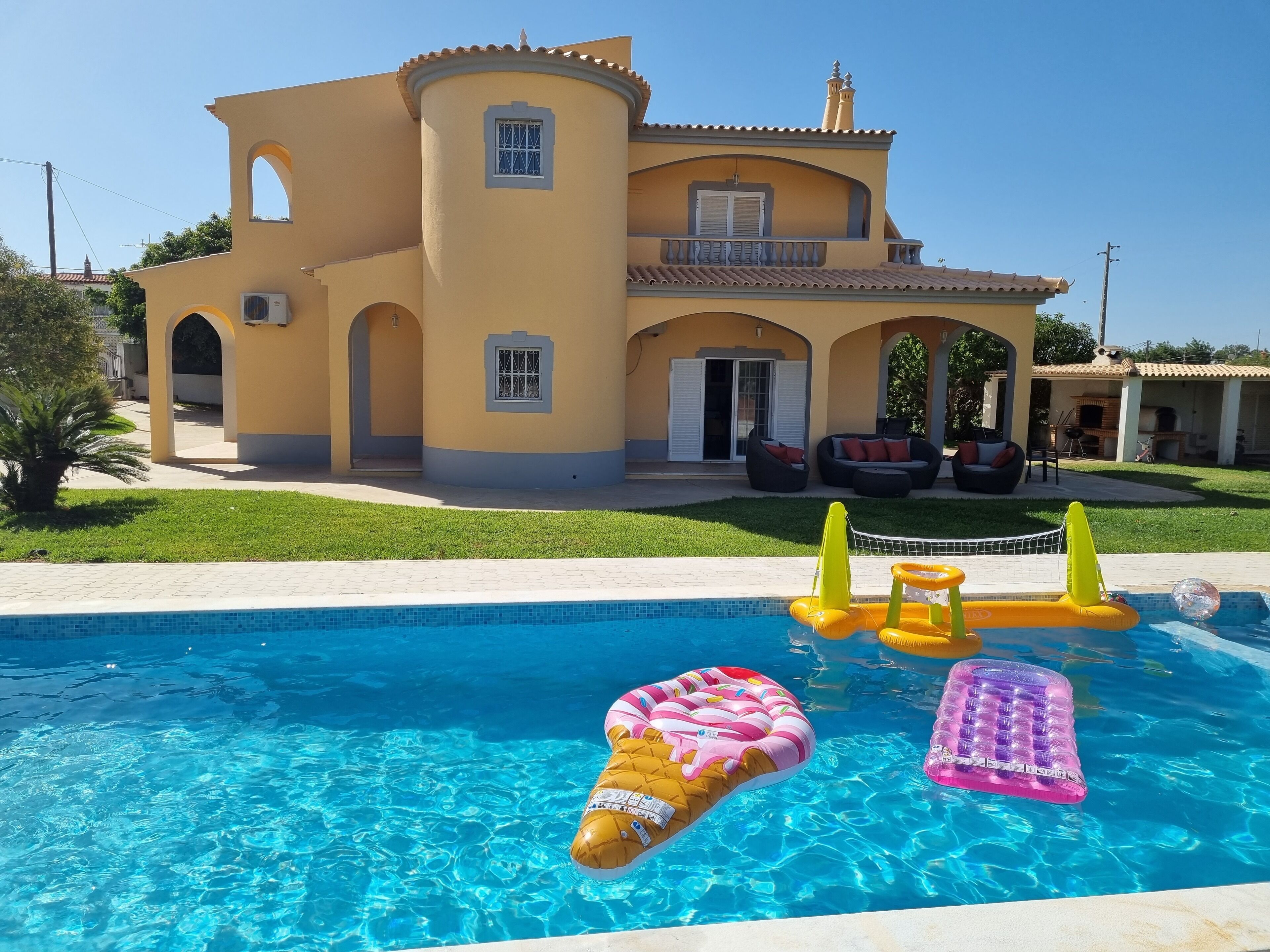 A pool with inflatable toys and a house with a yellow facade and arched windows.