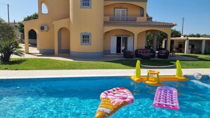 A pool with inflatable toys and a house with a yellow facade and arched windows. - 4 bedroom villa with private pool, 5 min from the beach, Wifi included (Moncarapacho)