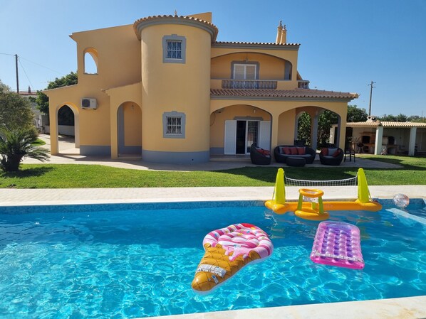 A pool with inflatable toys and a house with a yellow facade and arched windows.