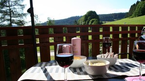 Eine Holzterrasse mit einem Tisch, der für eine Mahlzeit gedeckt ist, darunter Speisen in Schalen und Weingläser.