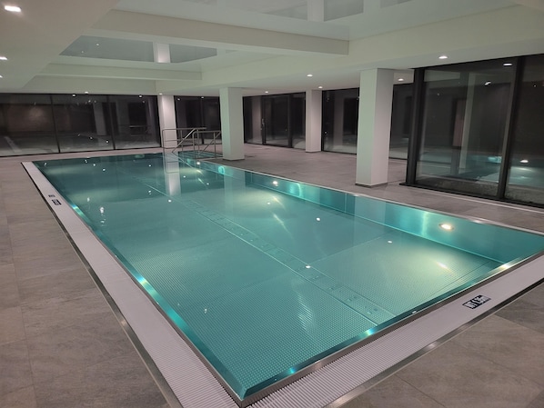 Una gran piscina interior con suelo de baldosas y barrera de cristal.