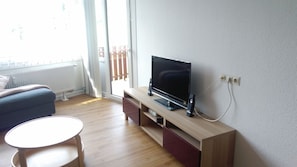 Una sala de estar con una televisión de pantalla plana sobre un mueble de madera, un sofá y una pequeña mesa redonda.