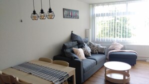 Ein modernes Wohnzimmer mit einem grauen Sofa, einem runden Couchtisch und einem Essbereich mit einer Tischläufer mit Streifen.