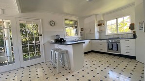 A kitchen with a central island, white cabinets, a stove, and a clock on the wall. - Allamanda House, 3 Willow Street (Crescent Head)