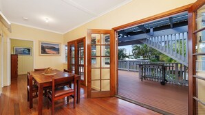 A dining area with a wooden table and chairs, a wooden door leading to a balcony with a wooden deck and railing. - Berry, 16 East Street (Crescent Head)