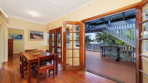 A dining area with a wooden table and chairs, a wooden door leading to a balcony with a wooden deck and railing. - Berry, 16 East Street (Crescent Head)
