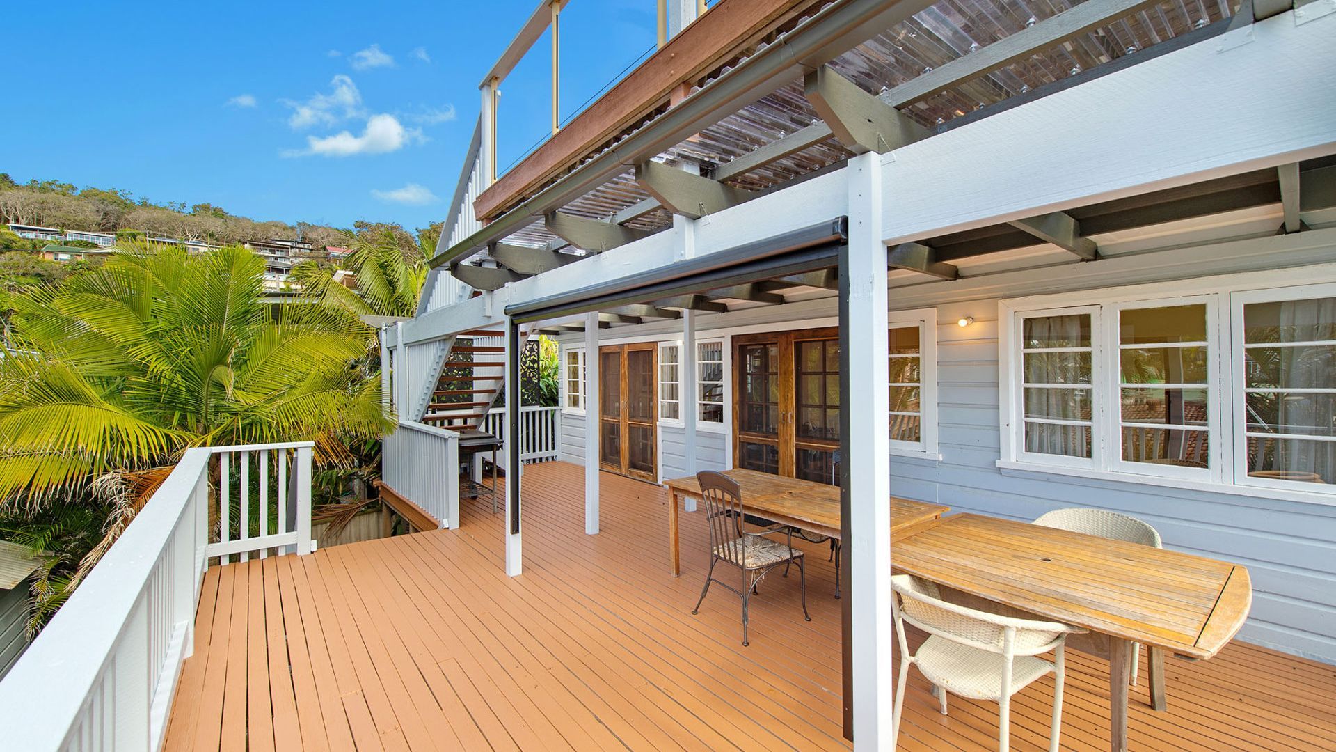 A wooden deck with a table and chairs, a covered area with windows, and a view of the surrounding landscape.
