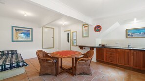 A kitchen with a dining table and chairs, wooden cabinets, and a tiled floor. - Berry, 16 East Street (Crescent Head)