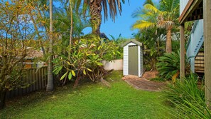 A well-maintained garden with a small shed, a wooden fence, and a variety of tropical plants.