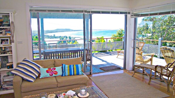 A room with a sofa, a coffee table, and a view of a deck with outdoor furniture.