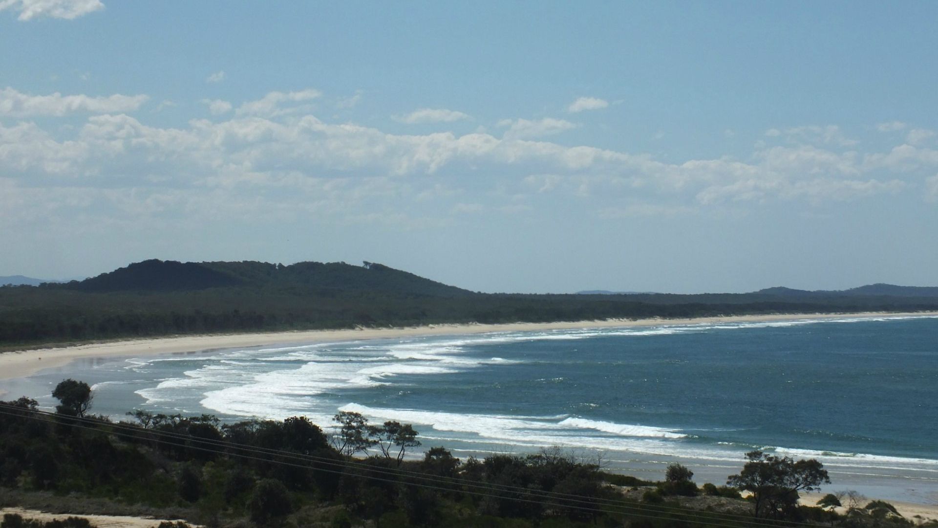 A coastal landscape with a beach, ocean waves, and a hill in the distance.
