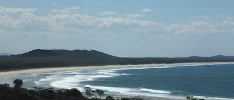 A coastal landscape with a beach, ocean waves, and a hill in the distance.