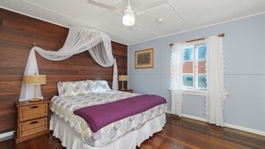 A bedroom with a bed, bedside lamps, a window with curtains, a ceiling fan, and a wooden wall.