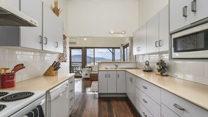 A modern kitchen with white cabinets, a stove, and a large window overlooking a scenic view.